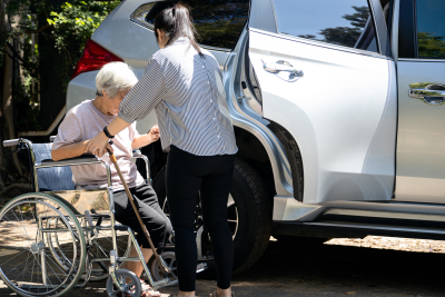 caregiver helping elderly woman in wheelchair to get into the car